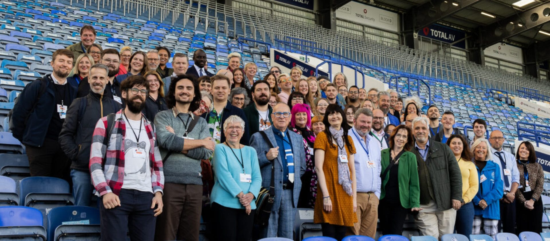 a large diverse group of people pose for the camera standing in the seating area of Portsmouth football club Portsmouth Creates | We Connect Conference | 2024 allies networks and organisations