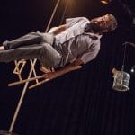 A man sitting on a chair bounces on a trampoline.