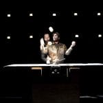 Two performers juggle props, with one standing behind the other.