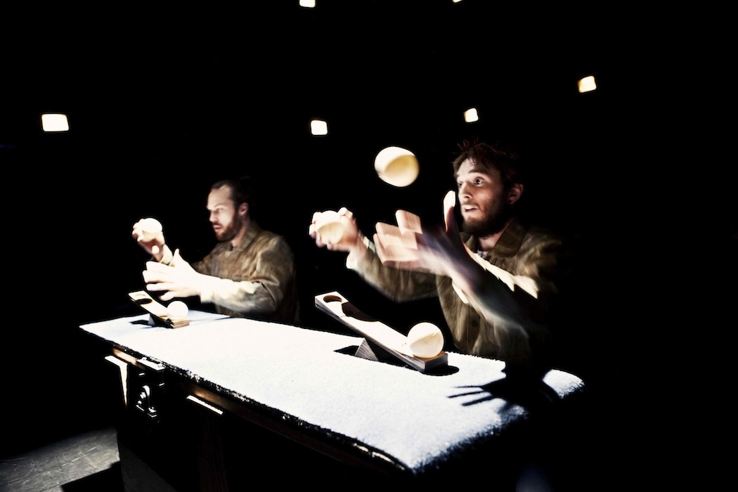 Two performers juggle props while sitting at a desk.