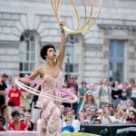 A performer twirling multiple hula hoops at an outdoor event with an audience in the background.