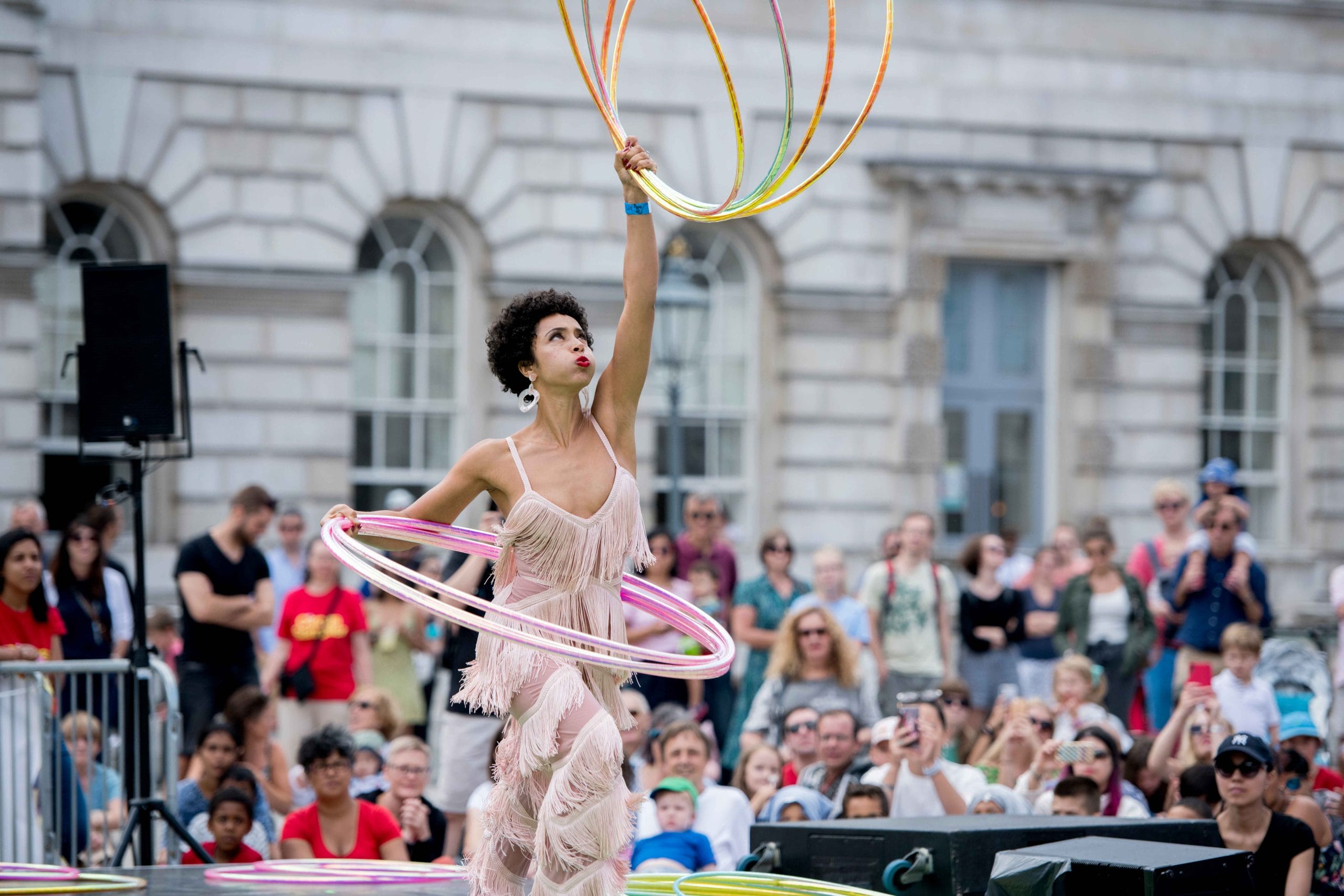 A performer twirling multiple hula hoops at an outdoor event with an audience in the background.