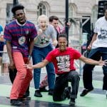 Group of dancers performing on stage with one person in the foreground in a dynamic pose.