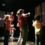 Children interact with digital projections on screens in a dark room.