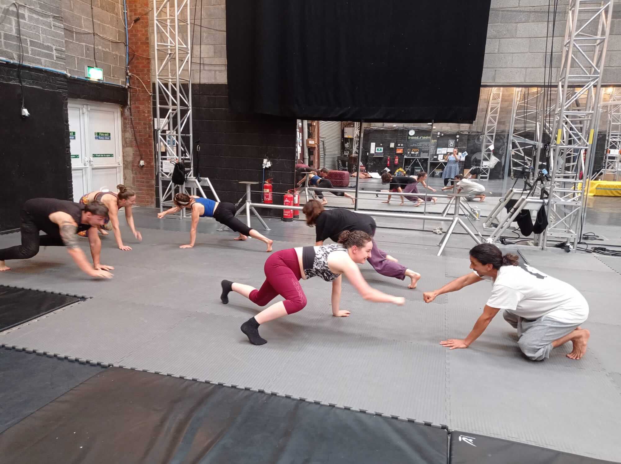 Group of people practicing acrobatics in a gym, with stage equipment visible in the background.