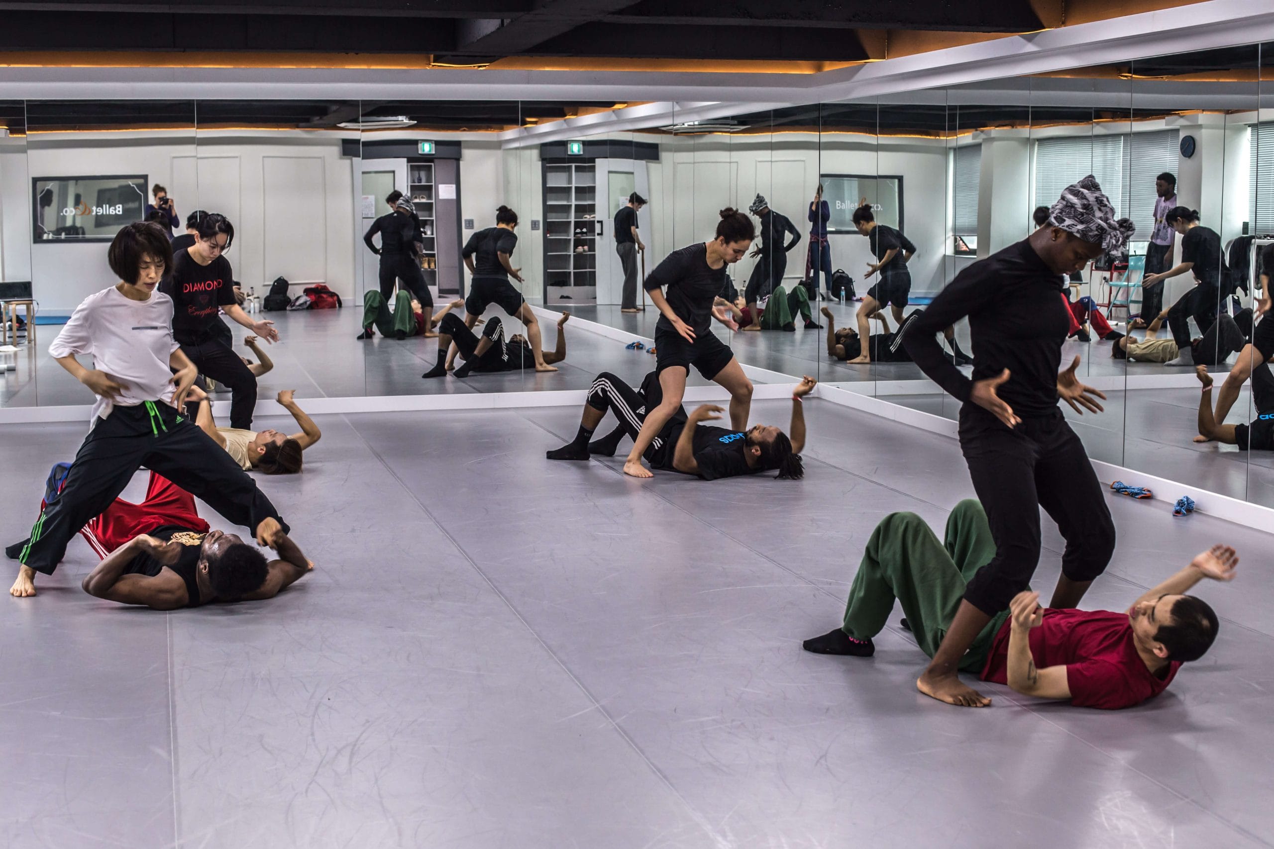 A dance class with participants practicing movements on a studio floor with mirrors.