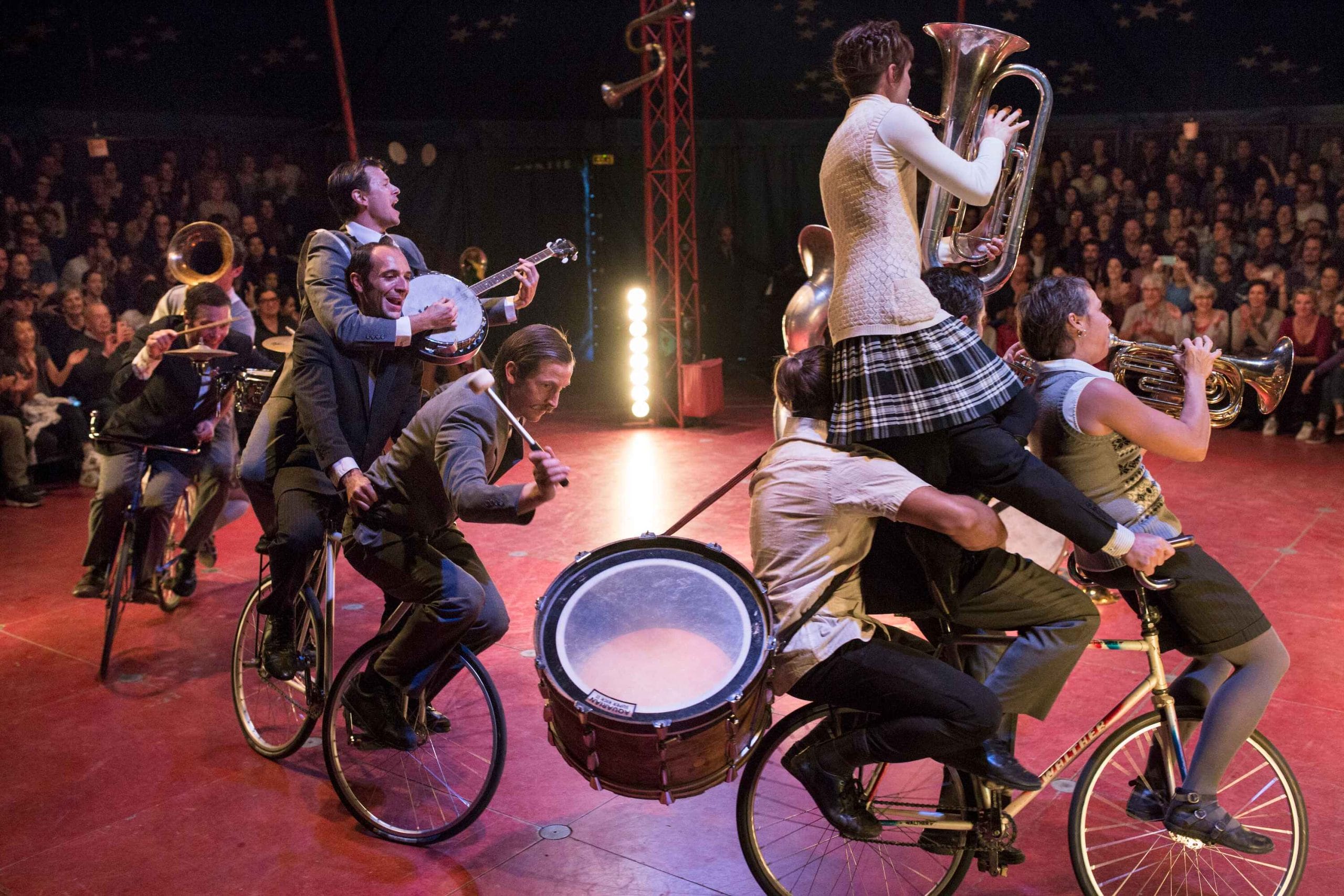 Performers playing musical instruments while riding bicycles in a circus setting.