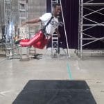 A performer hangs in mid-air during a harness-assisted stunt at a circus rehearsal.