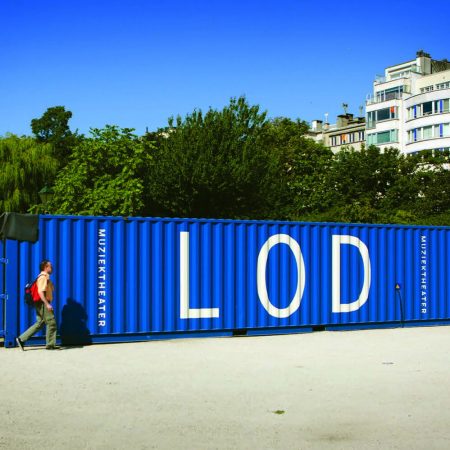 A blue shipping container arranged to spell 'LOD' in a park, with a person casually walking by.