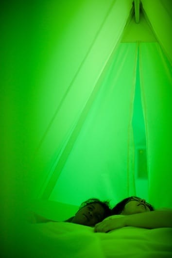 Two people lying down in a tent-like environment, bathed in green light.
