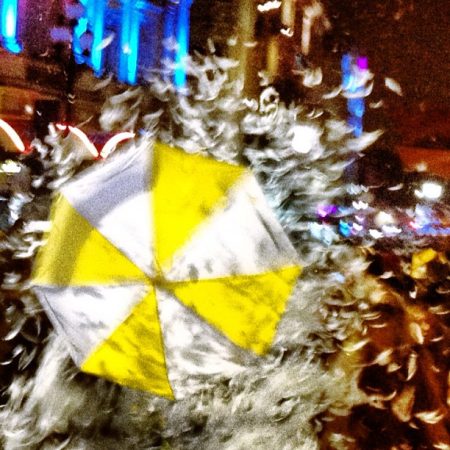 A yellow and white striped umbrella opening out to reveal a shower of white feathers blurred umbrella feathers | Piccadilly Circus Circus Crying Out Loud NPO
