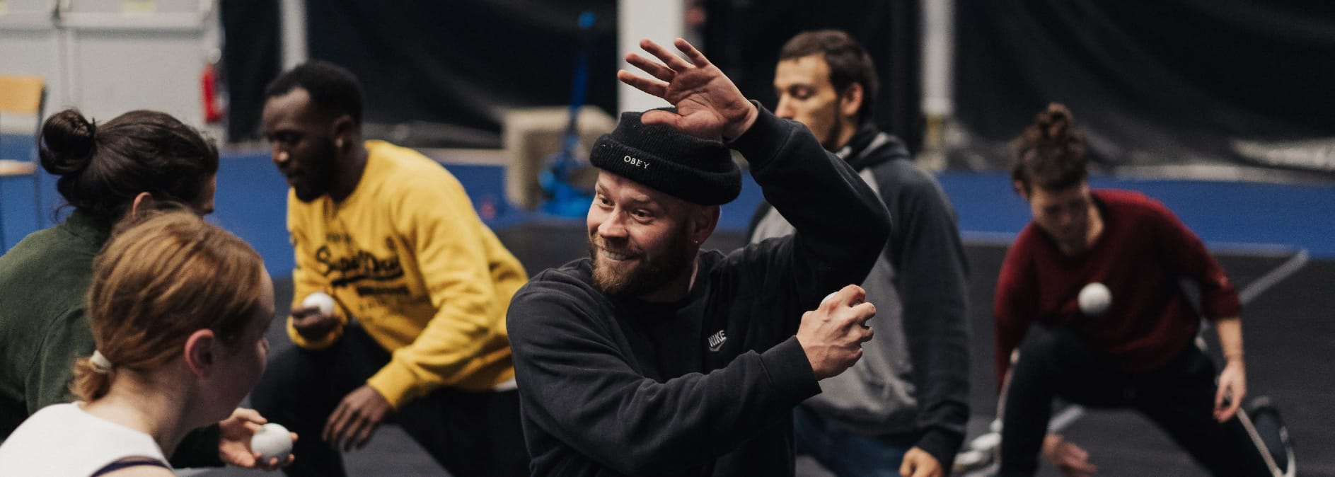 six performers in an indoor rehearsal space are pulling small white balls amongst each other