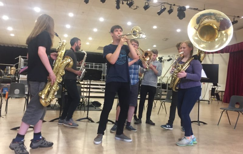 Groups of casually dressed brass musicians playing instruments indoors together Circa Tsuïca musical acrobats