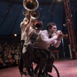 Five acrobats balance skilfully on a single bicycle under a circus tent.
