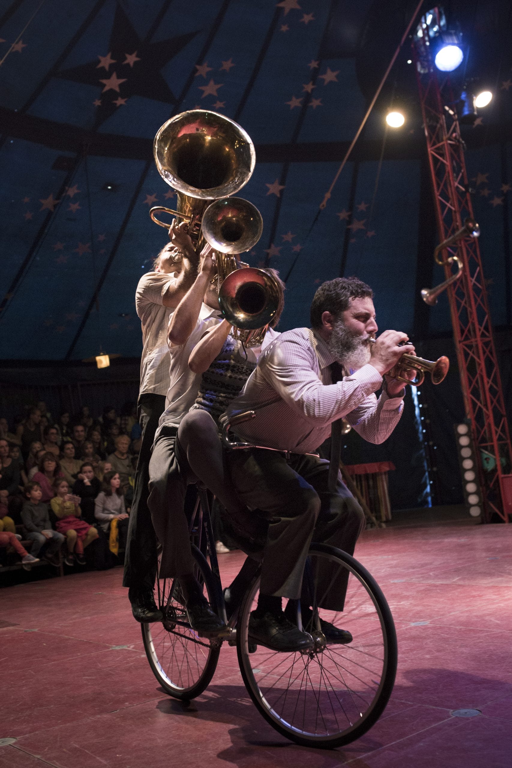 Five acrobats balance skilfully on a single bicycle under a circus tent.