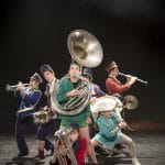 seven performing musicians stand in a group all dressed in colourful military band uniforms playing instruments including a tuba and a drum Opus 7 | Circa Tsuica @ Vincent Beaume