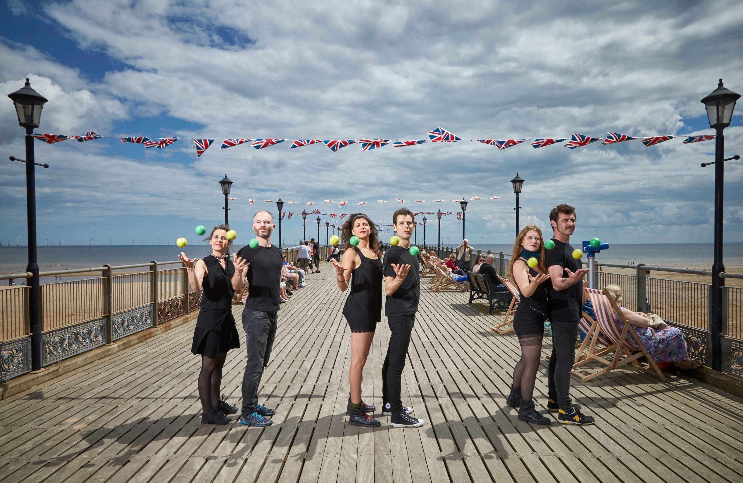 A group of people juggling on a scenic pier decorated with British flags.