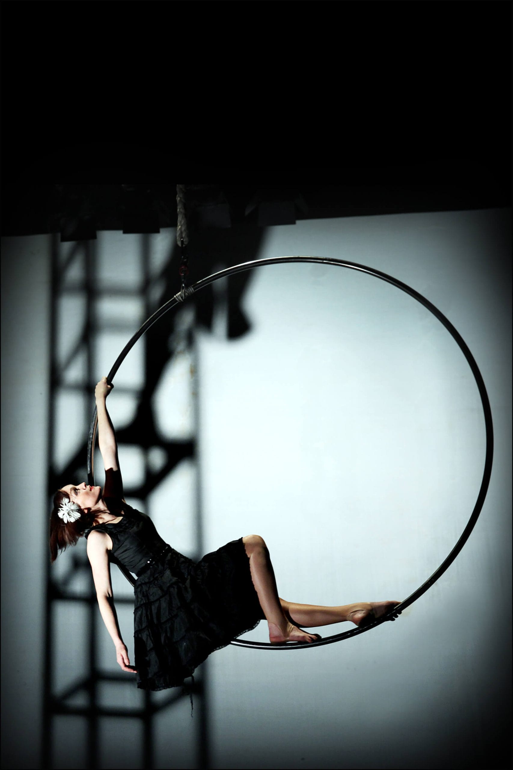 Person performing an aerial hoop act with dramatic lighting and shadows.