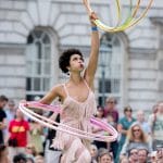 A performer twirling multiple hula hoops at an outdoor event with an audience in the background Marawa | Circus Sampler © Camilla Greenwell
