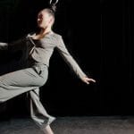 two hair hanging artists both dressed in grey trouser suits swing by their hair on a dark indoor stage