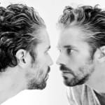 head and shoulders, brightly lit black and white photo of bearded white man with short dark and greying hair wearing a white round necked t-shirt and looking themselves very closely in a mirror James Thierrée Richard Haughton