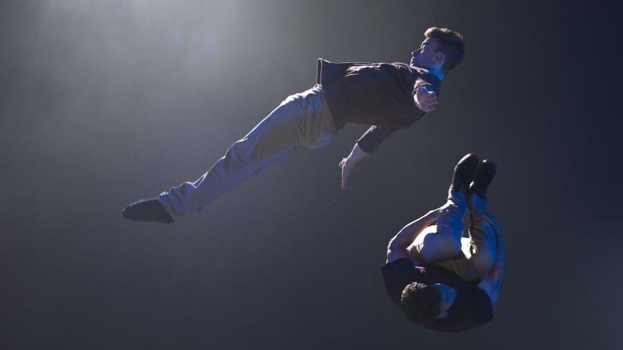 Two acrobats perform a dynamic mid-air stunt in a dimly lit room, showcasing strength, balance, and precision.