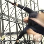 A blurred athlete performs an acrobatic move on a metal structure with agility, demonstrating intense physical training.