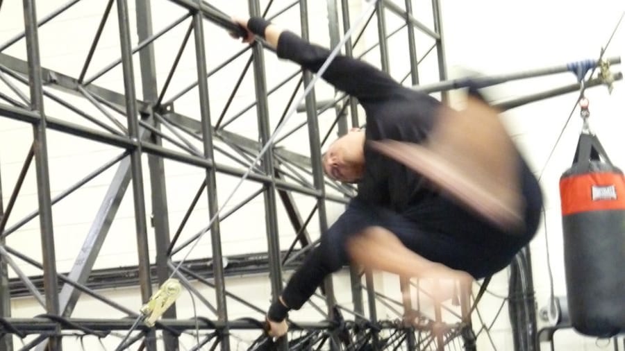 A blurred athlete performs an acrobatic move on a metal structure with agility, demonstrating intense physical training.