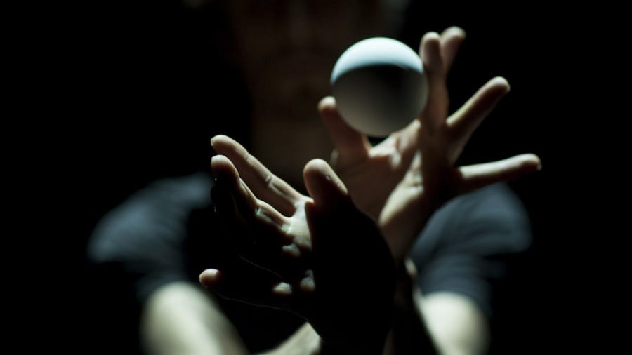 A person’s hands are gracefully poised in a dark setting, skilfully catching a white ball with a sense of motion and intense focus.