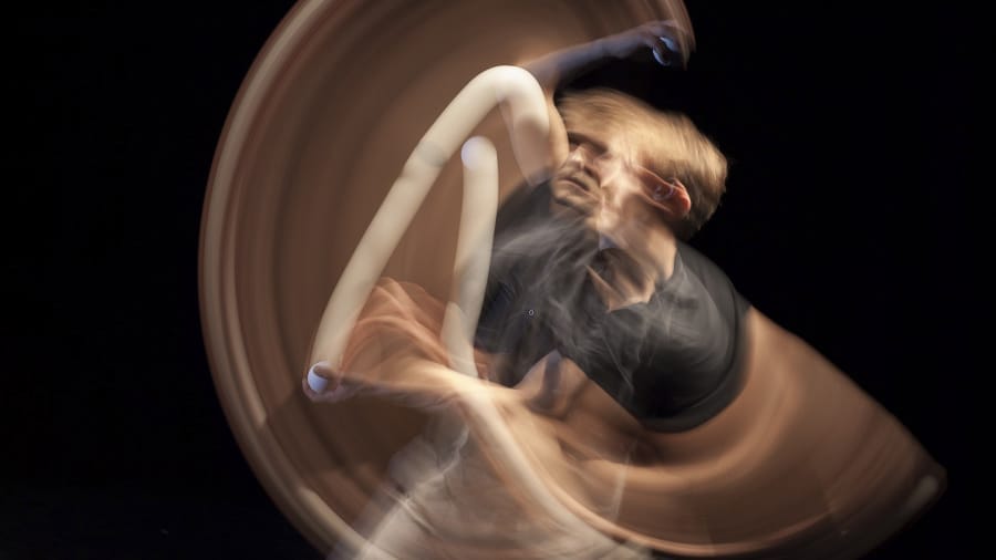 A dynamic motion blur captures a juggler in mid-performance, with arms gracefully swirling and flowing against a dark background.