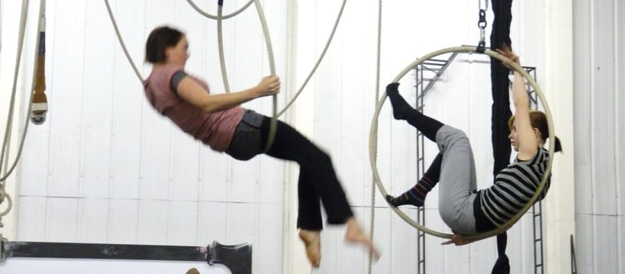 Two acrobats perform on aerial ropes and hoops, swinging elegantly in an indoor rehearsal space. The Blender Project