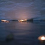 a paper boat floats on water in nighttime with a lit candle in it reflects life-changing journeys