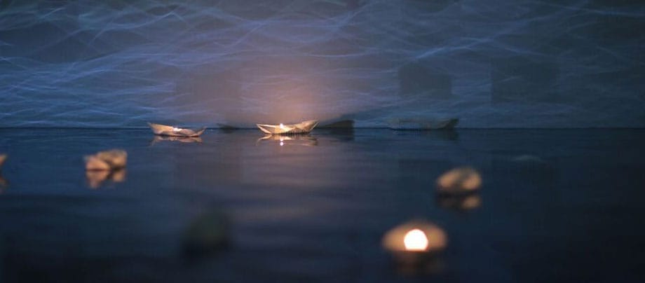 a paper boat floats on water in nighttime with a lit candle in it reflects life-changing journeys