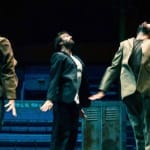 Three performers in suits energetically jump on a trampoline in a circus setting.