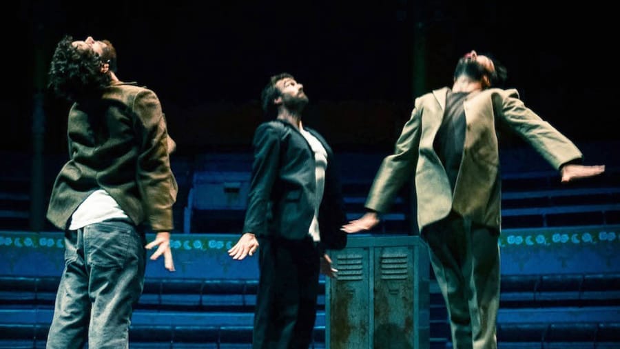 Three performers in suits energetically jump on a trampoline in a circus setting.
