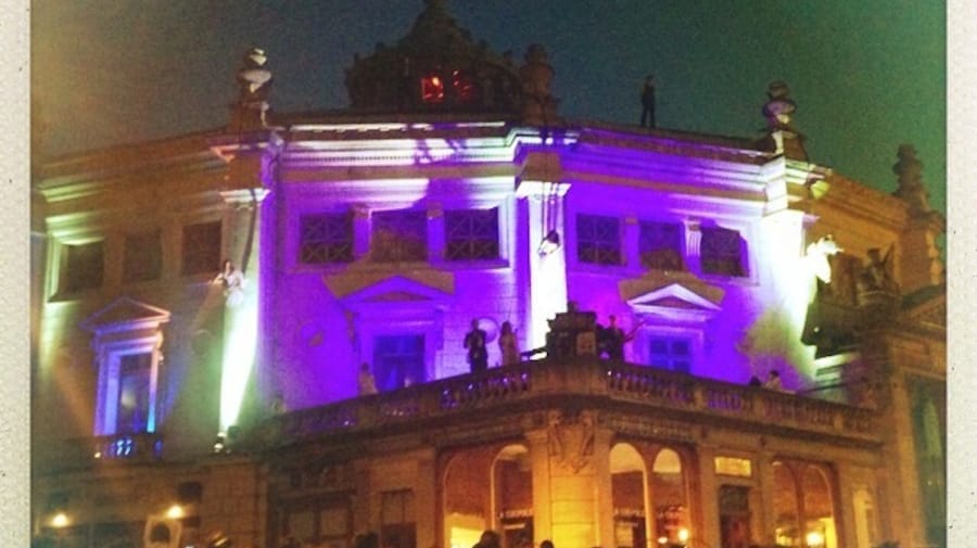 Illuminated historic building at night, featuring purple lights and people on the roof, creating a festive atmosphere.