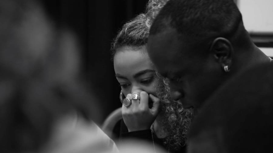 Black and white photography of two individuals engaging in a play reading rehearsal, surrounded by blurred figures Vex | Simon Parker © Hannah Blakeston Lodge