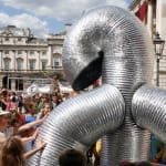 an abstract creature made from silver corrugated flexible piping performs to a large outdoor audience in the Somerset House courtyard, the children in the audience tentatively touch the creature Free Time | Somerset House