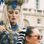 an elaborately dressed and made-up hairstylist concentrates on building a fun hair structure on a willing audience member, against the outdoor brickwork of Somerset House courtyard Free Time Somerset House