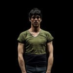 A performer in a fitted green shirt stands confidently against a dark backdrop