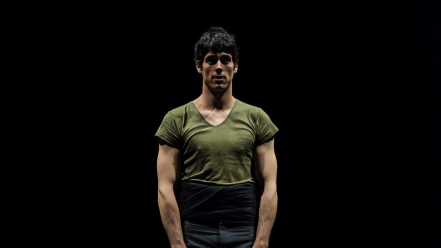 A performer in a fitted green shirt stands confidently against a dark backdrop