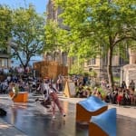 Performers all dressed in casual costumes, move in harmony on an outdoor stage against a cathedral, green trees and blue sky Solent Artist Inspiration Trip