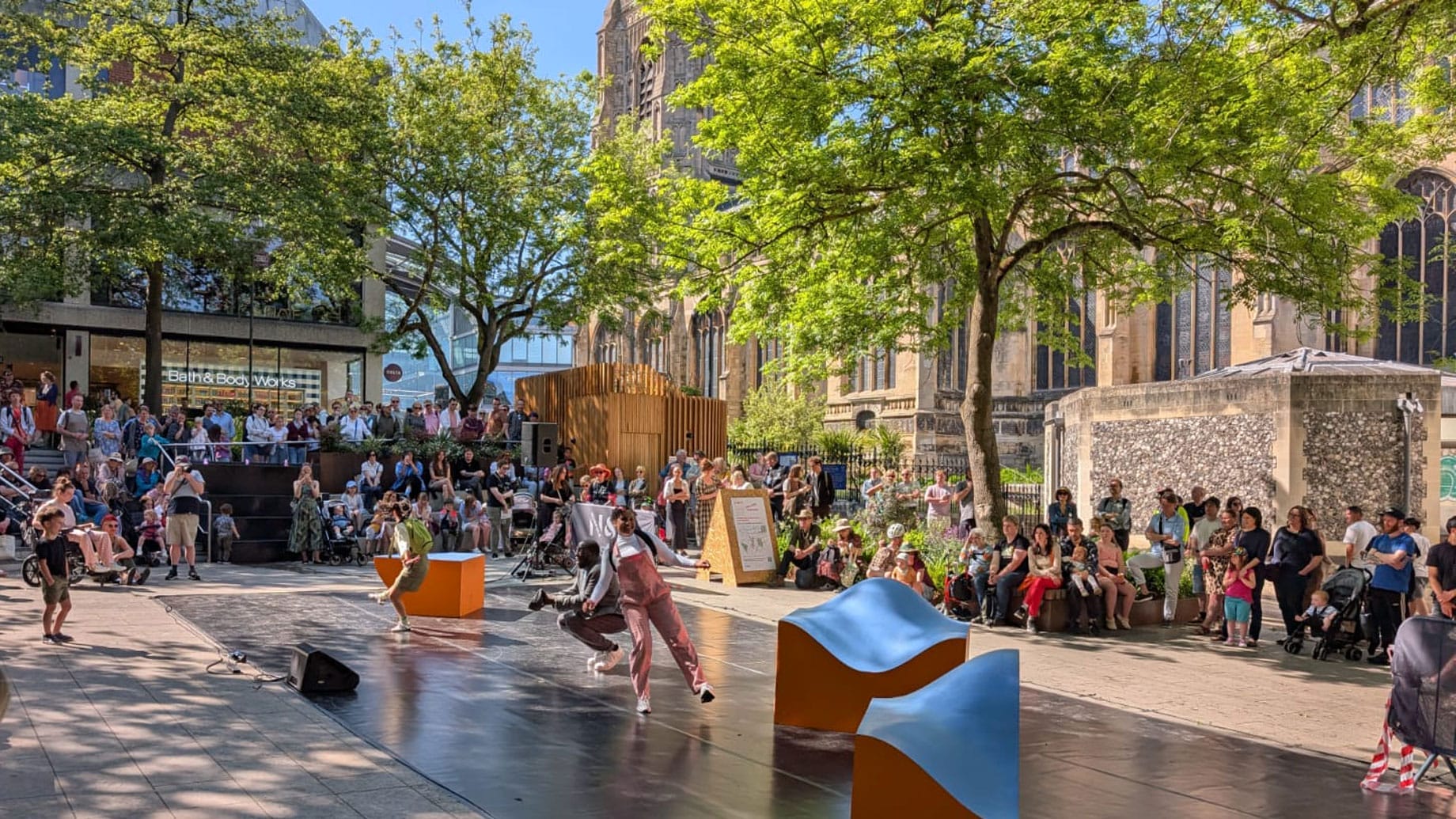 Performers all dressed in casual costumes, move in harmony on an outdoor stage against a cathedral, green trees and blue sky Solent Artist Inspiration Trip