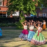 Three performers dressed in a coloured skirts and white shirts, all move in harmony in an outdoor green park Solent Artist Inspiration Trip