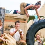 four performers in an outdoor setting, two play with a large tyre, one holds a brown sack and the fourth eats from a small bowl, they all wear autumnal colours with either braces or dungarees Farm Yard Circus | Morning