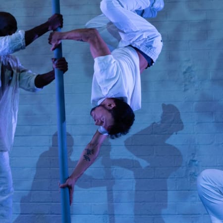 four dancers on an indoor, blue-lit stage, they all wear white casual costumes, two central performers hold a Chinese pole and perform on it, one upside-down, the other two performers kneel as they look on incl in four dancers on an indoor, blue-lit stage, they all wear white casual costumes, two central performers hold a Chinese pole and perform on it, one upside-down, the other two performers kneel as they look on incl in summer 2024 activity round-up Birds show Kundle Cru Birds show Kundle Cru