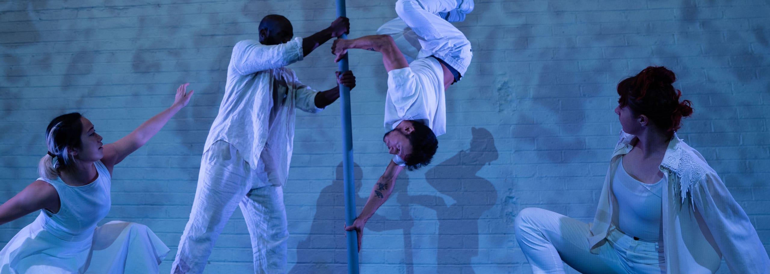 four dancers on an indoor, blue-lit stage, they all wear white casual costumes, two central performers hold a Chinese pole and perform on it, one upside-down, the other two performers kneel as they look on incl in four dancers on an indoor, blue-lit stage, they all wear white casual costumes, two central performers hold a Chinese pole and perform on it, one upside-down, the other two performers kneel as they look on incl in summer 2024 activity round-up Birds show Kundle Cru Birds show Kundle Cru